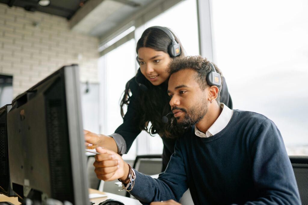 Two call center employees working together with headsets in a modern office setting.